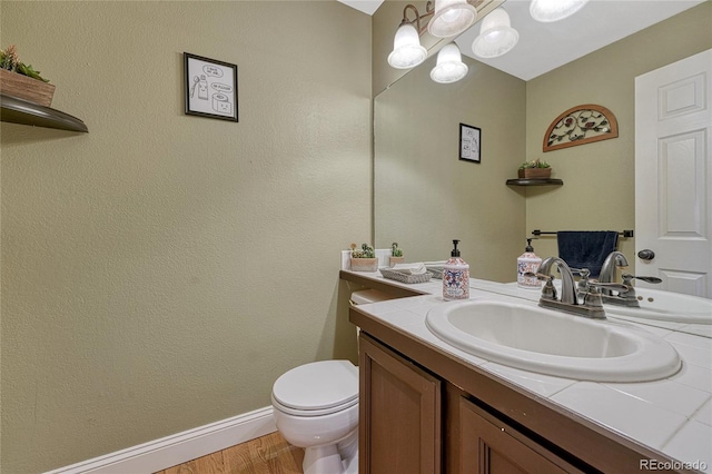 half bath featuring toilet, vanity, baseboards, and wood finished floors