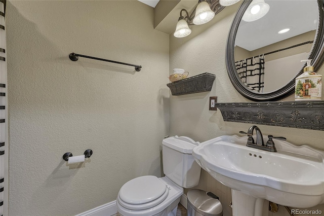 bathroom featuring a sink, toilet, and a textured wall