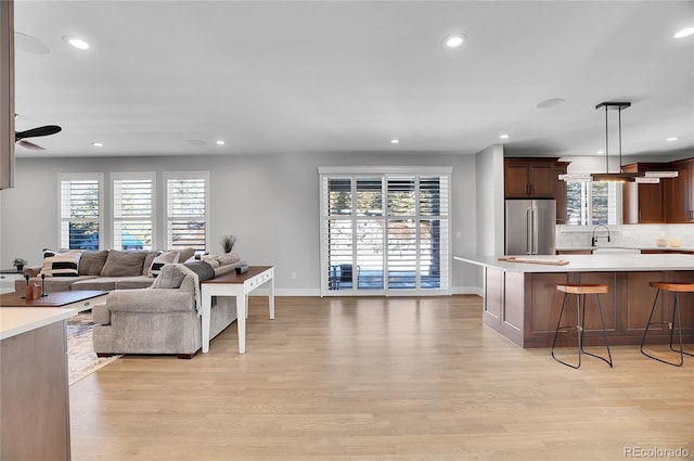 kitchen with a breakfast bar, sink, high end refrigerator, light wood-type flooring, and pendant lighting