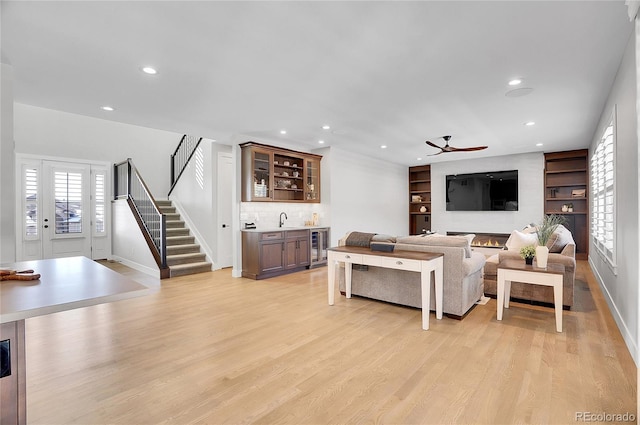 living room with built in features, ceiling fan, indoor wet bar, beverage cooler, and light wood-type flooring