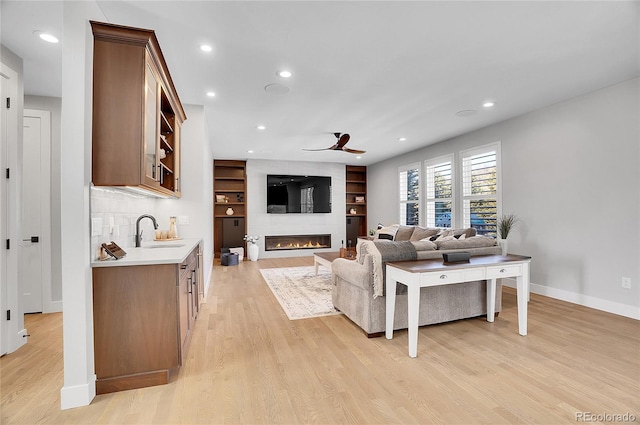 living room featuring ceiling fan, sink, a large fireplace, and light wood-type flooring