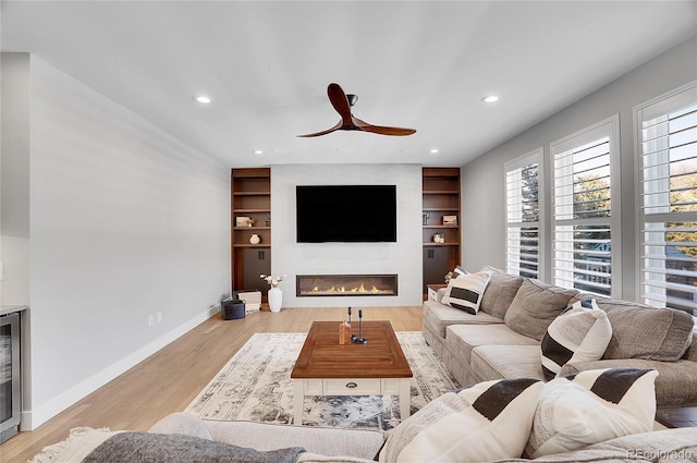 living room featuring light hardwood / wood-style flooring, built in shelves, a fireplace, and ceiling fan