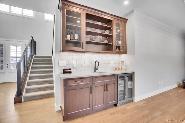 bar featuring wine cooler, sink, tasteful backsplash, and light wood-type flooring