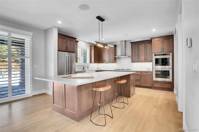 kitchen featuring a kitchen island, appliances with stainless steel finishes, tasteful backsplash, hanging light fixtures, and wall chimney exhaust hood