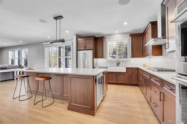 kitchen with a kitchen island, appliances with stainless steel finishes, decorative light fixtures, sink, and light hardwood / wood-style flooring