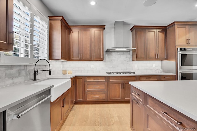 kitchen with sink, decorative backsplash, light hardwood / wood-style floors, stainless steel appliances, and wall chimney exhaust hood