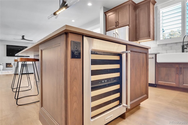 kitchen with wine cooler, a breakfast bar, sink, light hardwood / wood-style flooring, and decorative backsplash