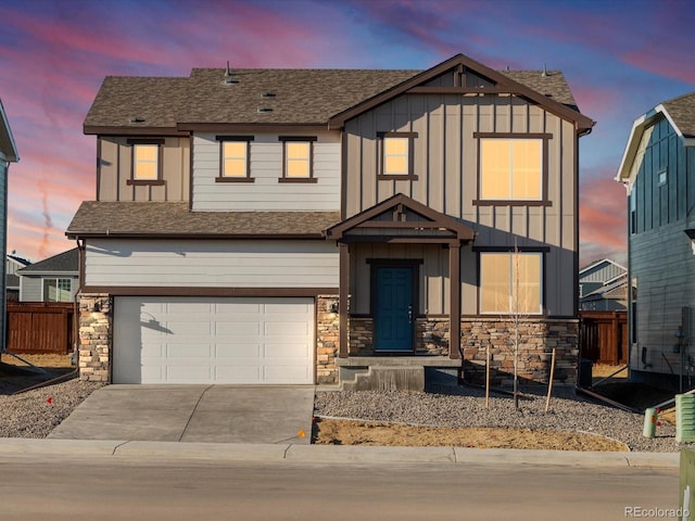 view of front of property featuring an attached garage, fence, driveway, stone siding, and board and batten siding