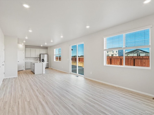 unfurnished living room with light wood-type flooring, baseboards, and recessed lighting