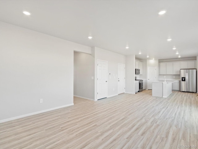 unfurnished living room with recessed lighting, a sink, light wood-style flooring, and baseboards