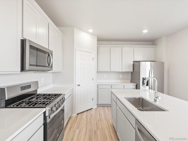 kitchen with light countertops, light wood-style flooring, appliances with stainless steel finishes, white cabinets, and a sink