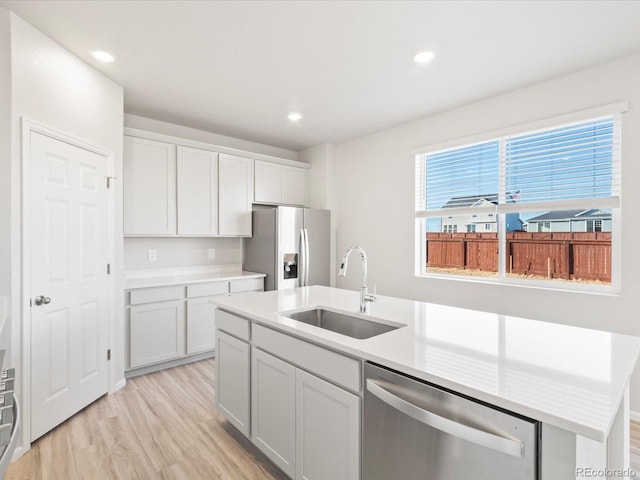 kitchen featuring a kitchen island with sink, stainless steel appliances, light countertops, light wood-style floors, and a sink