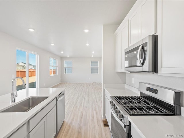 kitchen featuring stainless steel appliances, a sink, light countertops, and light wood-style floors