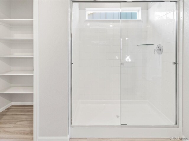 full bathroom featuring a shower stall, a spacious closet, baseboards, and wood finished floors