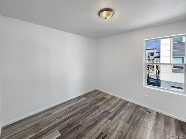 empty room featuring wood finished floors, visible vents, and baseboards