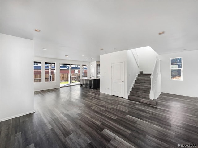 unfurnished living room with baseboards, dark wood finished floors, stairs, recessed lighting, and a sink