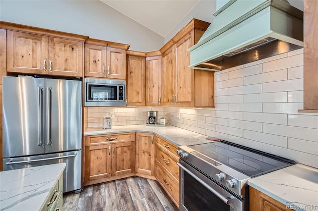 kitchen with light stone countertops, stainless steel appliances, decorative backsplash, vaulted ceiling, and custom range hood