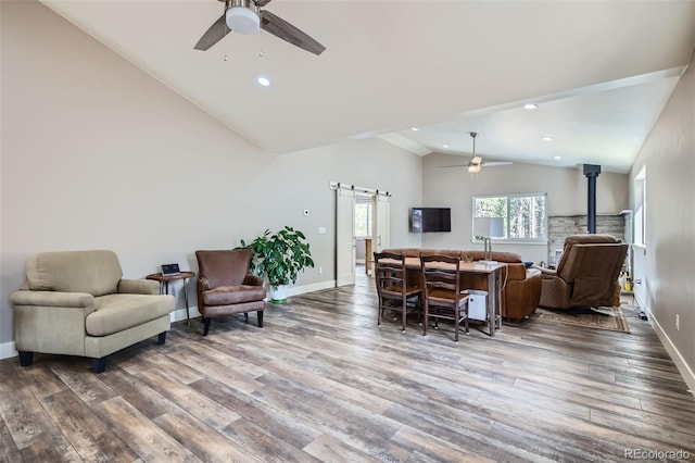 living room featuring wood finished floors, a barn door, baseboards, ceiling fan, and a wood stove