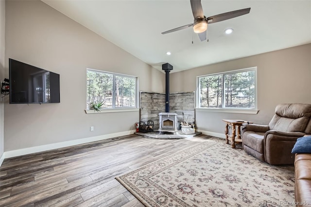 living area featuring baseboards, a wood stove, lofted ceiling, and wood finished floors