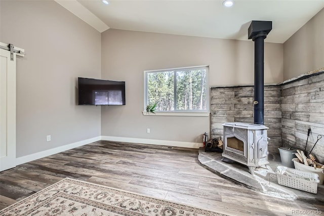 unfurnished living room with a barn door, a wood stove, wood finished floors, and lofted ceiling