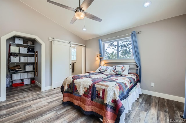 bedroom featuring baseboards, wood finished floors, a barn door, and vaulted ceiling