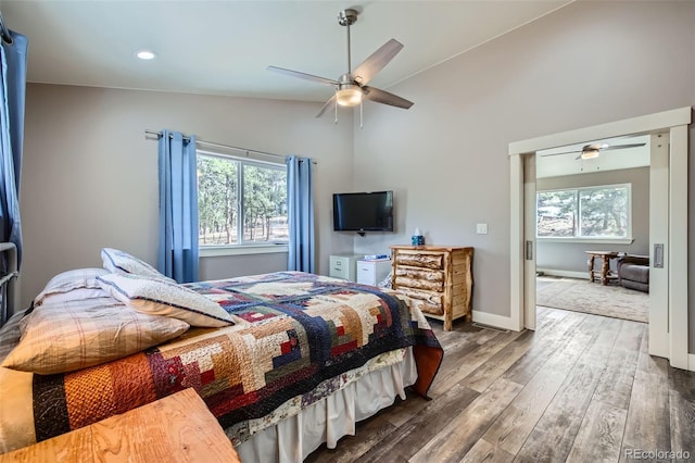 bedroom with vaulted ceiling, multiple windows, baseboards, and wood finished floors