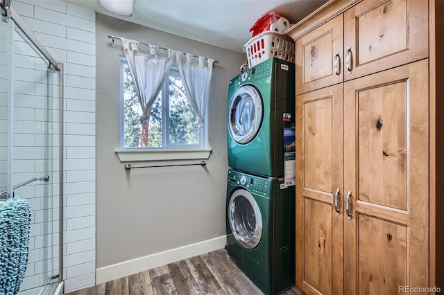 washroom featuring dark wood-type flooring, stacked washer / dryer, cabinet space, and baseboards