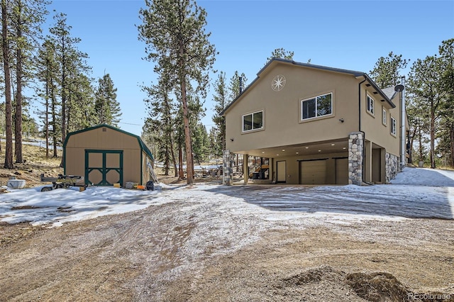 exterior space with a shed, stucco siding, a carport, driveway, and an outbuilding