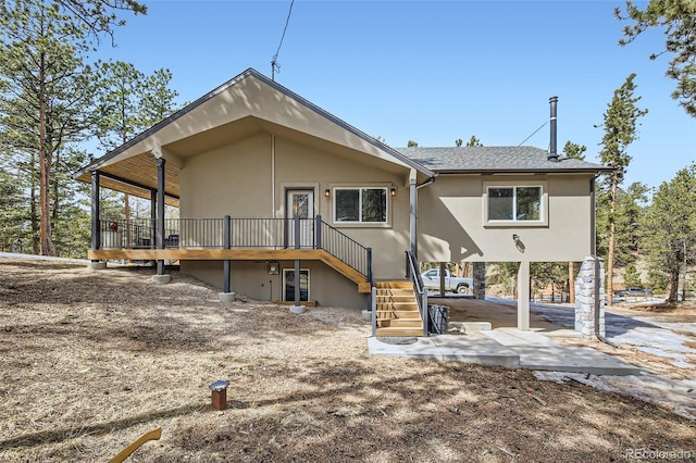 rear view of house featuring stucco siding, a patio, stairway, a shingled roof, and a wooden deck