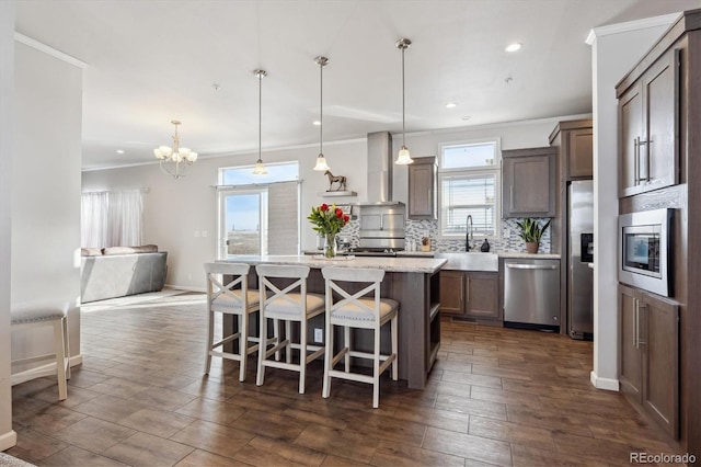 kitchen with stainless steel appliances, a center island, sink, wall chimney range hood, and decorative light fixtures