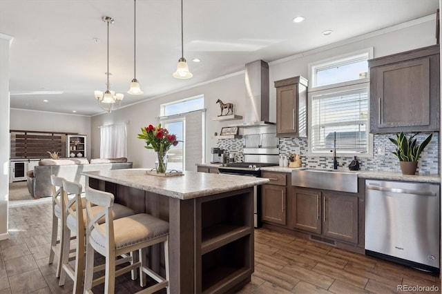 kitchen featuring wall chimney exhaust hood, a center island, decorative light fixtures, stainless steel appliances, and sink