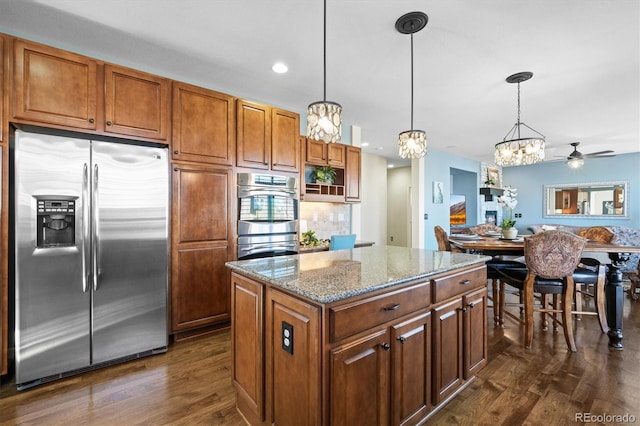 kitchen featuring light stone counters, a center island, dark wood-style flooring, decorative light fixtures, and stainless steel appliances