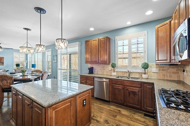 kitchen featuring dark wood-style floors, a center island, light stone countertops, stainless steel appliances, and a sink