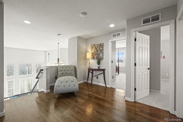 sitting room with a chandelier, visible vents, an upstairs landing, and wood finished floors