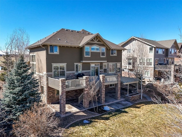 rear view of house with stone siding, a yard, a deck, and a patio