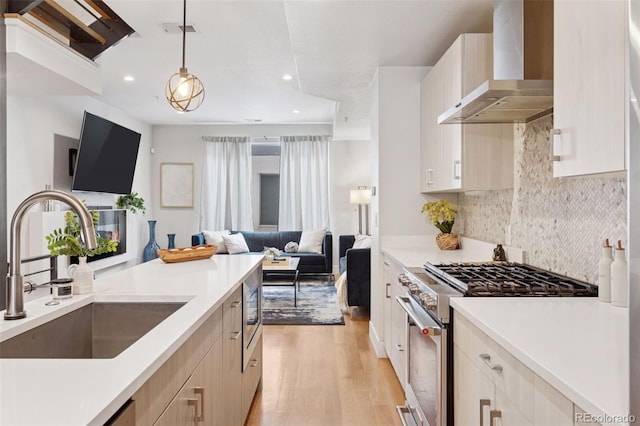 1836 Grove St Unit 108, Denver, CO 80204 - kitchen featuring stainless steel stove, wall chimney exhaust hood, a sink, open floor plan, and light wood-style flooring