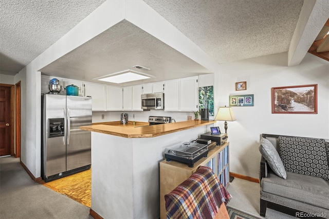 kitchen featuring stainless steel appliances, white cabinets, a textured ceiling, and kitchen peninsula