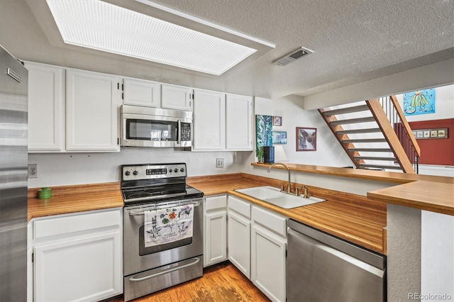 kitchen with sink, white cabinetry, a textured ceiling, light wood-type flooring, and appliances with stainless steel finishes