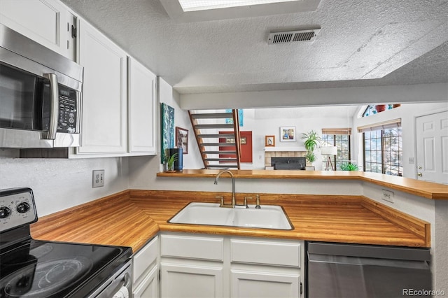 kitchen with sink, stainless steel appliances, a textured ceiling, white cabinets, and kitchen peninsula