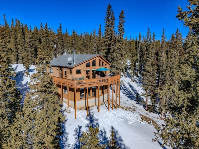 snow covered property featuring a forest view and a wooden deck