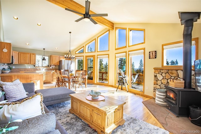 living room featuring a ceiling fan, a wood stove, high vaulted ceiling, light wood-type flooring, and beamed ceiling