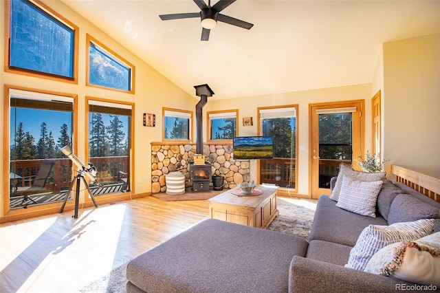 living area with high vaulted ceiling, a wood stove, ceiling fan, and wood finished floors