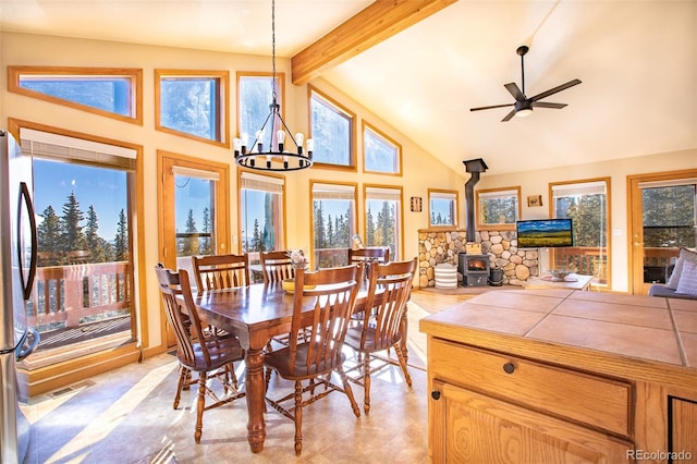 dining area featuring visible vents, beamed ceiling, a wood stove, high vaulted ceiling, and ceiling fan with notable chandelier