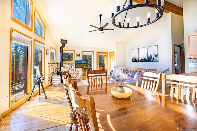 dining area with a wood stove, light wood-style flooring, high vaulted ceiling, and ceiling fan