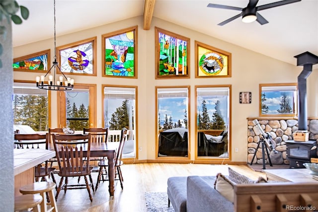 dining area with a wood stove, wood finished floors, high vaulted ceiling, beamed ceiling, and ceiling fan with notable chandelier