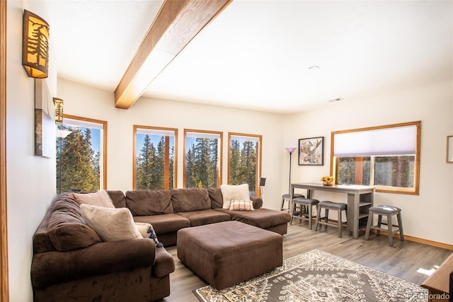 living room featuring light wood finished floors, beamed ceiling, visible vents, and baseboards