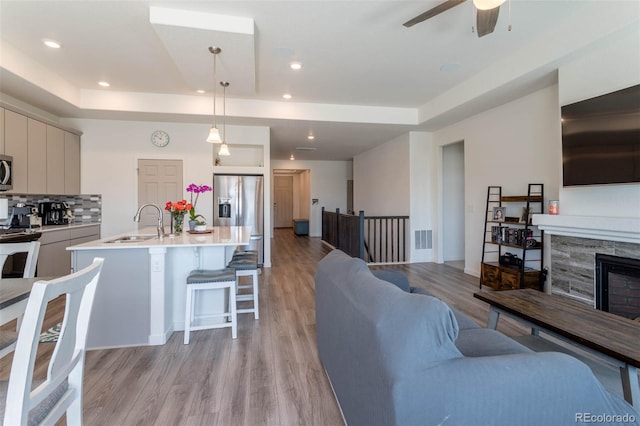 living room with a tray ceiling, sink, ceiling fan, and light hardwood / wood-style flooring