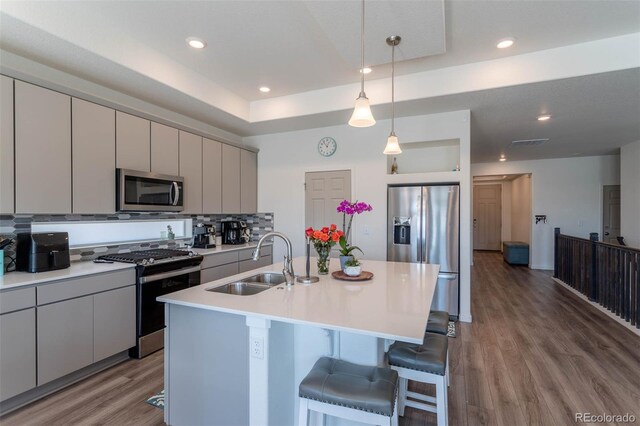 kitchen featuring a center island with sink, appliances with stainless steel finishes, wood-type flooring, pendant lighting, and sink