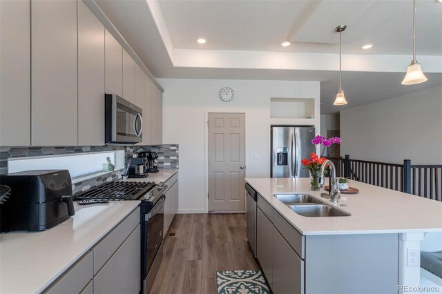 kitchen featuring a center island with sink, stainless steel appliances, hardwood / wood-style floors, decorative light fixtures, and sink