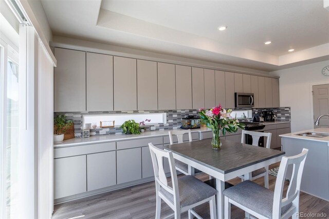 kitchen featuring sink, a tray ceiling, tasteful backsplash, and light hardwood / wood-style flooring